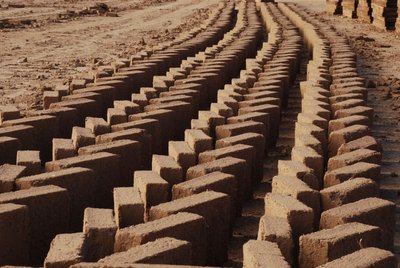 The image showcases rows of freshly made bricks laid out to dry in an arid landscape. The bricks are