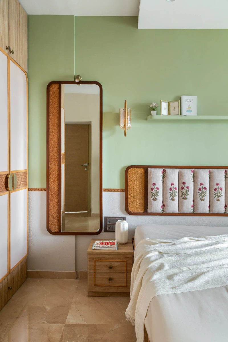 The primary bedroom is enveloped in a material palette that is inviting of nature. A combination of sage green, wood, rattan textures and floral prints brings a soothing vibe. Anuja Kambli