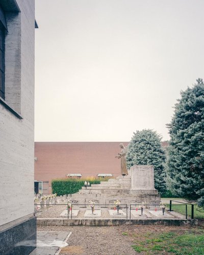 This architectural image captures a serene cemetery scene. A statue stands atop a stepped monument, 