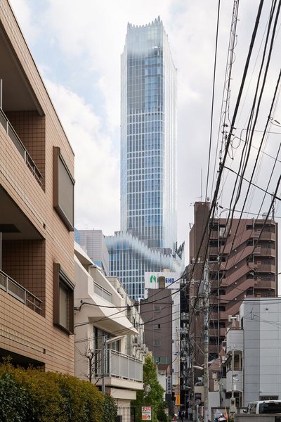 This architectural image showcases a modern skyscraper rising above a dense urban landscape. The sky