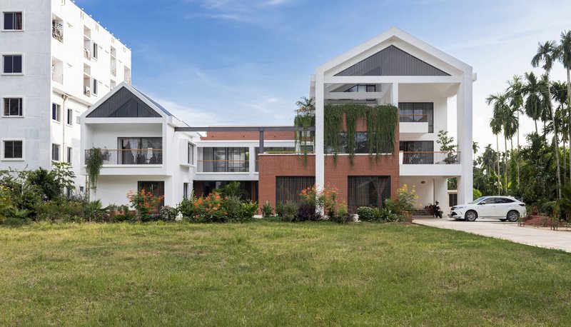 Street view of clustered white-framed gable volumes with red brick base and palm trees in the background