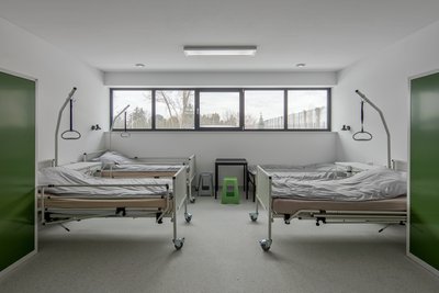 This image depicts a modern hospital room with a minimalist design. The room features two hospital b