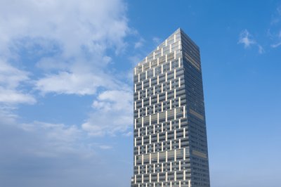 The image showcases a modern skyscraper with a distinctive geometric facade, set against a backdrop 