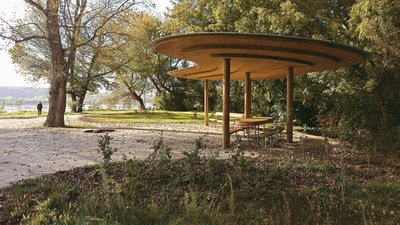 This architectural image showcases a modern pavilion in a park setting. The pavilion features a circ
