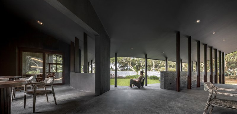 Long interior view of the covered terrace with a row of dark columns and a lone seated figure