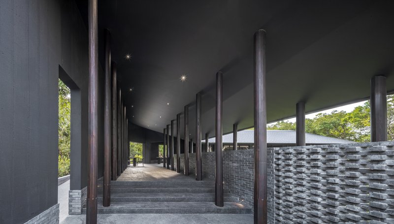 Stepped arrival walkway with tall dark columns and grey brick screen walls