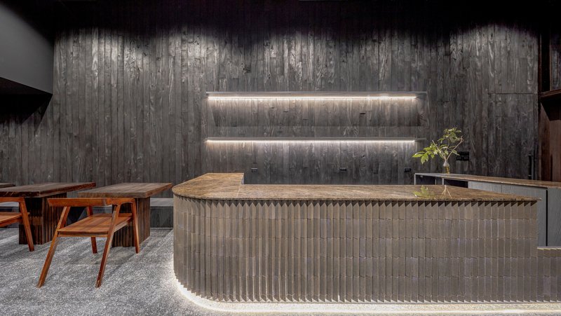 Bar counter detail with a fluted grey brick base and lit niche shelving behind