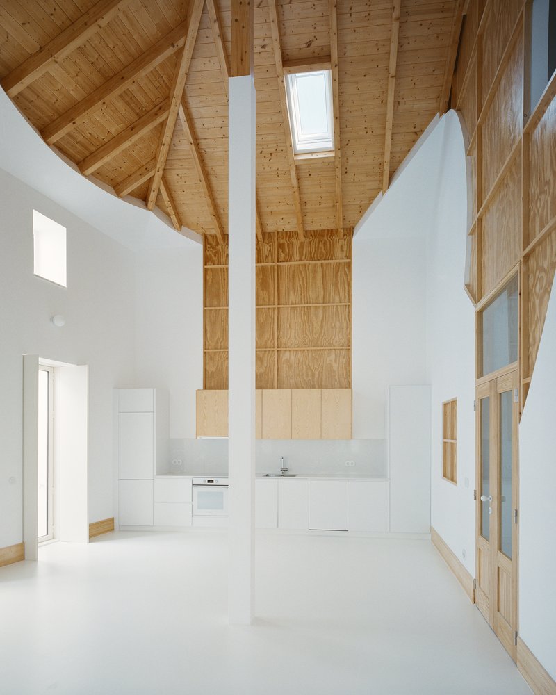Open kitchen below the pine ceiling with a tall plywood feature wall and central pillar