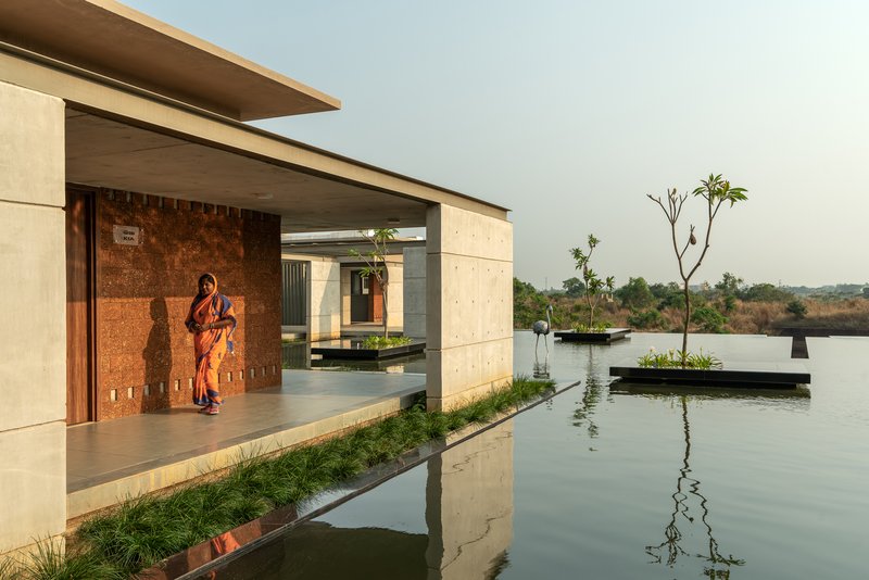 Open veranda facing a still reflecting pool with a sari-clad figure standing in shadow