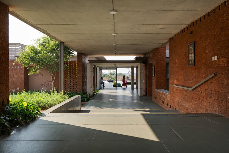Long covered colonnade with concrete ceiling and a red laterite wall on one side