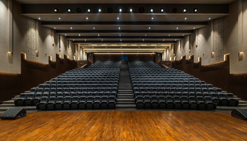 Auditorium interior with tiered black seating under a dark coffered ceiling