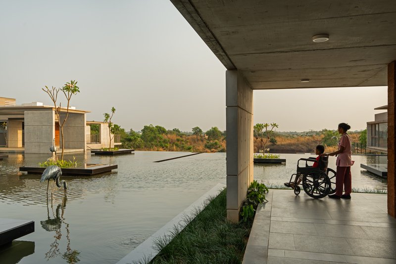 A patient in a wheelchair with an attendant looking across the reflecting pool from a covered walkway