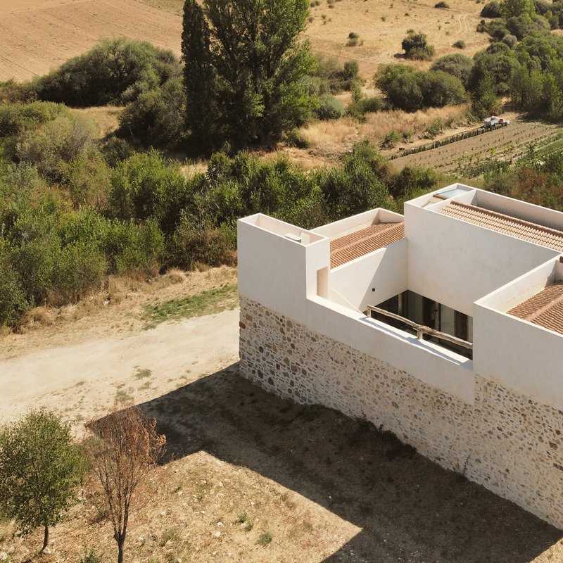 Drone shot of the new white volume rising above the original stone walls toward the surrounding fields