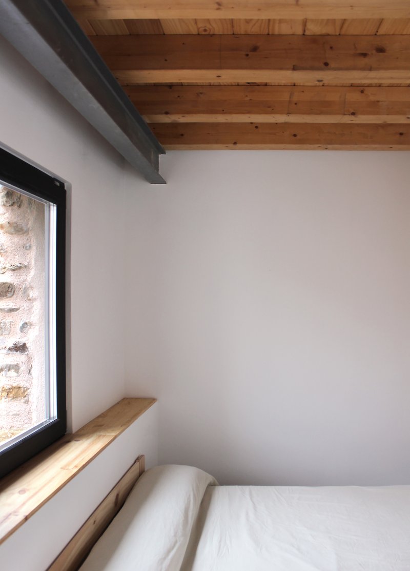 Bedroom corner with a framed window cut into the original stone wall and a timber sill