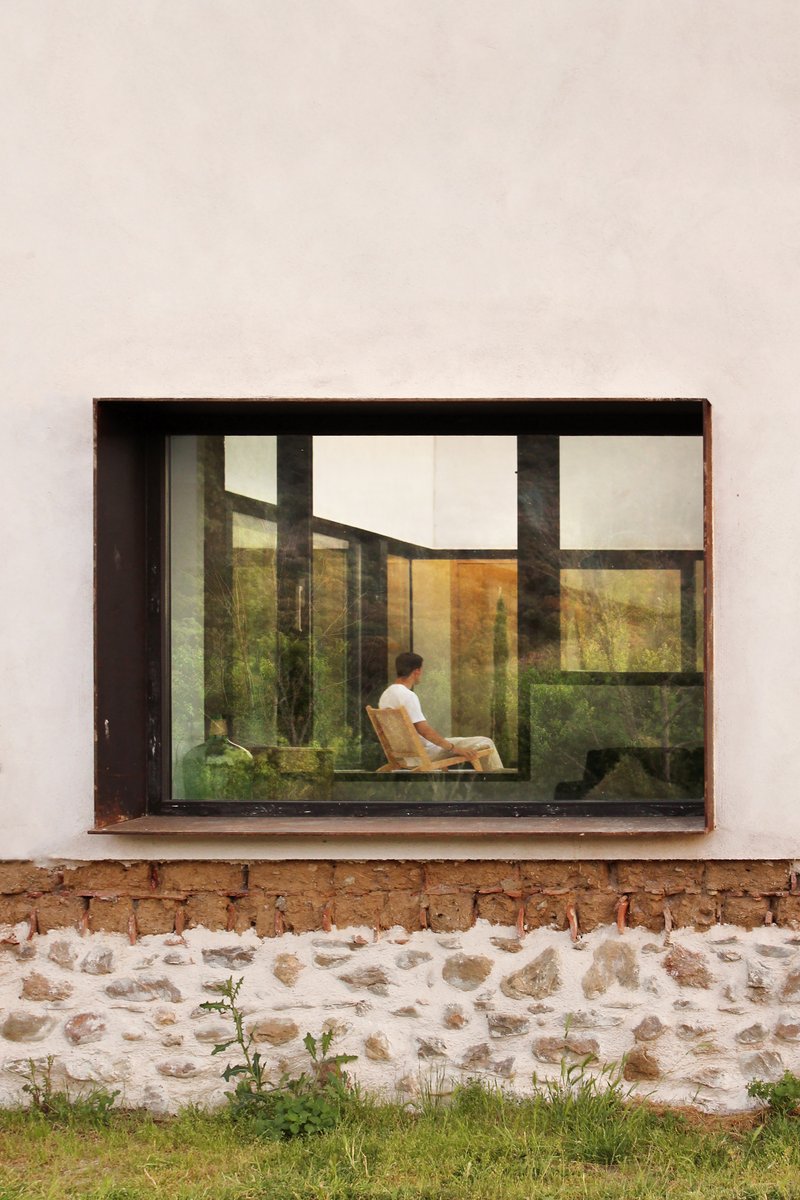 Reflection of the courtyard caught in a corten-framed window in the side wall