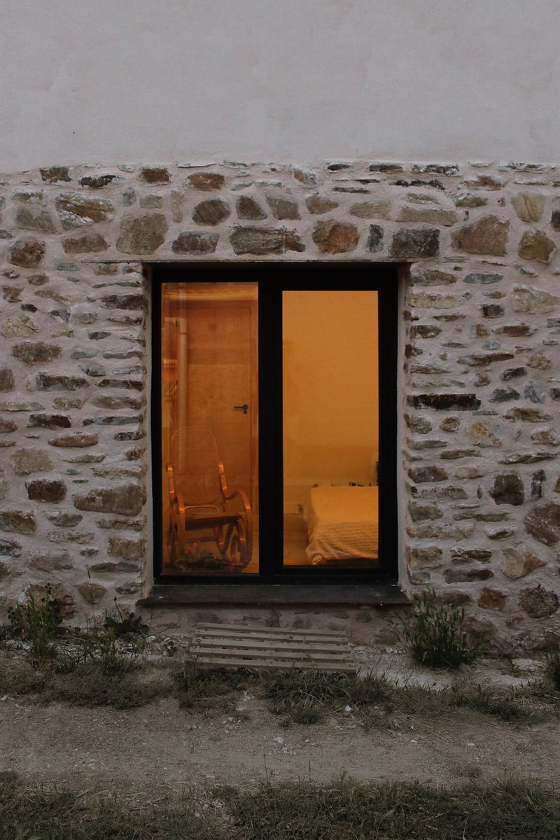 Stone facade window at dusk with the warm interior glowing through the glass