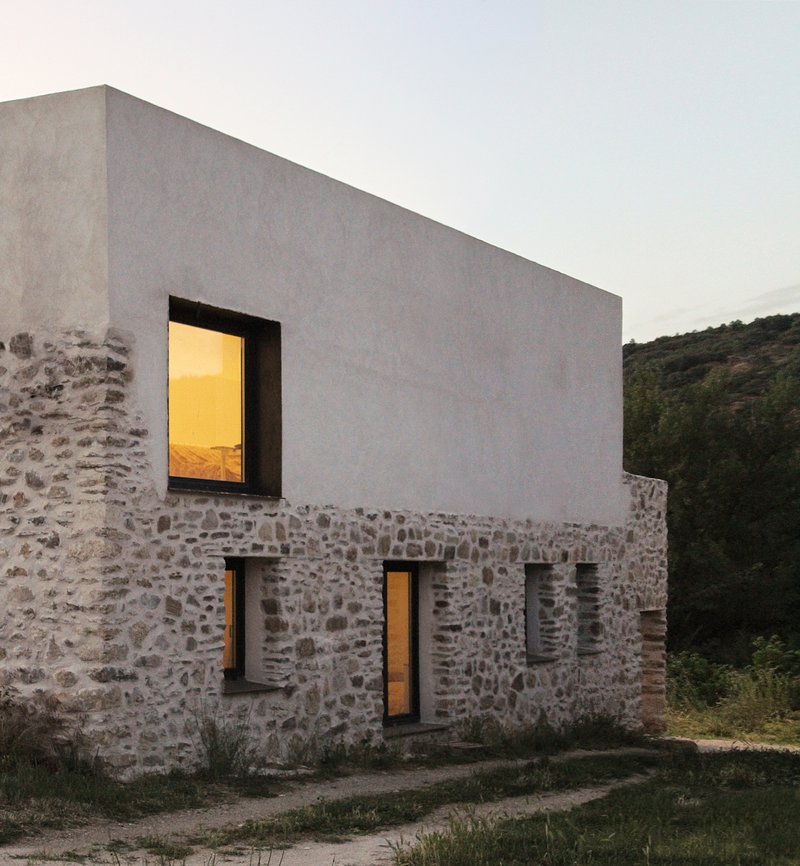 Dusk elevation showing the house lit from inside with the white volume above the stone base