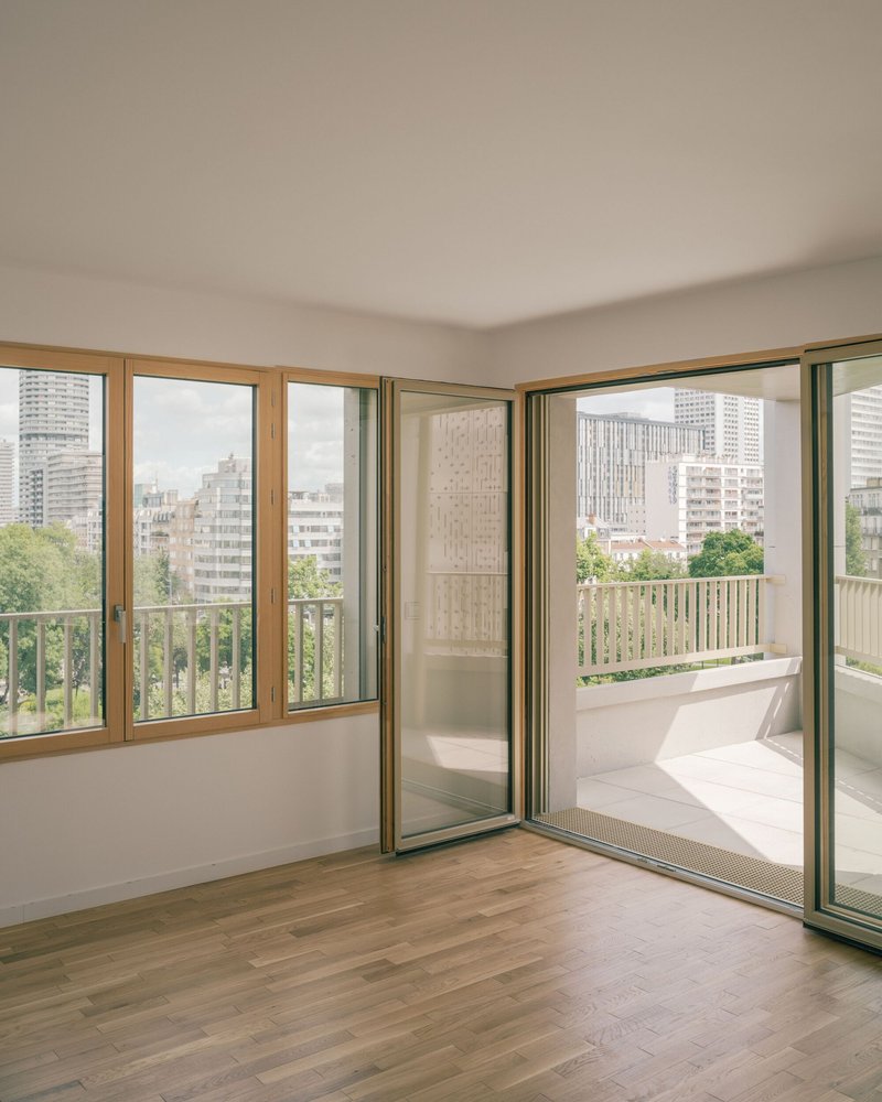 Empty family flat with timber-framed corner windows opening onto a long balcony with views over Paris