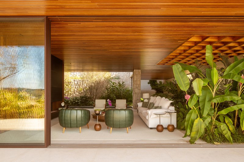 Living lounge with green leather pouffes, a low timber coffered canopy and glass walls opening to the garden