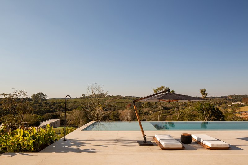 Pool deck with a single umbrella and two white sun loungers looking out toward the hills