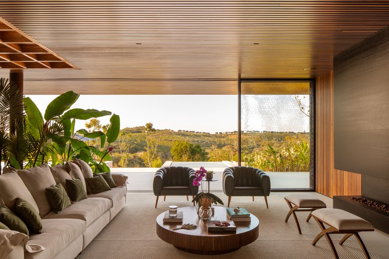 Living room with a fabric sofa, two dark armchairs and a fully glazed wall framing the distant hills