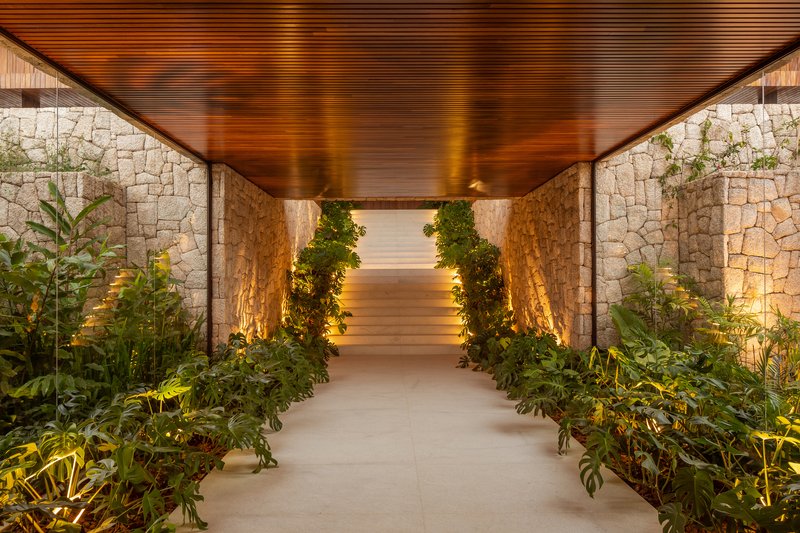 Narrow entry passage between stone walls leading into the house with integrated planting along both sides