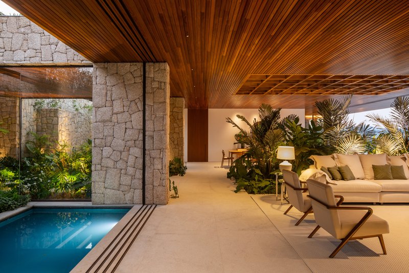 Indoor plunge pool beside a rough stone wall with a timber slatted ceiling and a lounge area beyond
