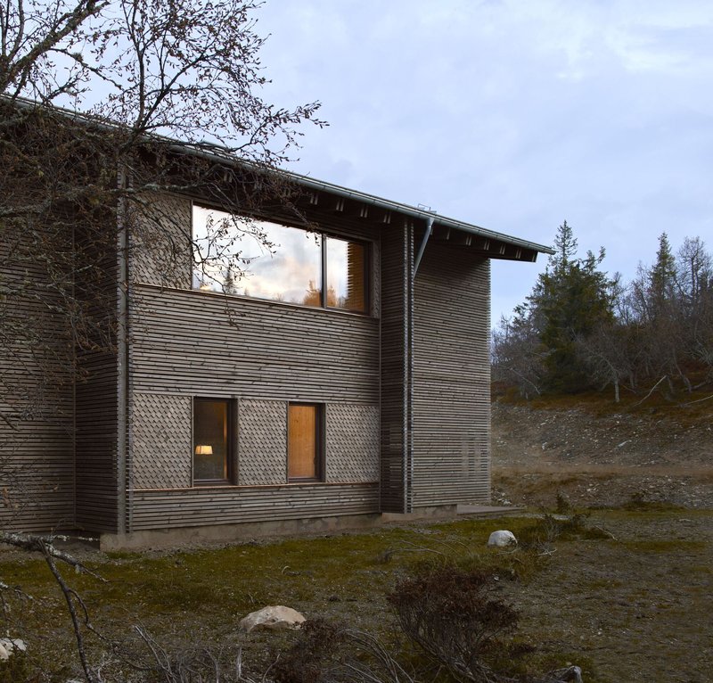 Side view at dusk with the upper living room glowing behind panoramic glazing